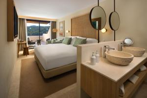 a bedroom with a bed and a bathroom with a sink at Cala San Miguel Ibiza Resort, Adults only, Curio Collection by Hilton in Puerto de San Miguel