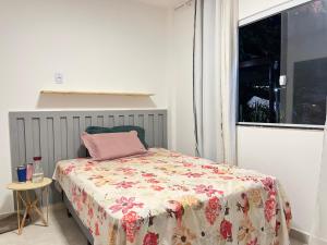 a bedroom with a bed with a flowered blanket and a window at Casa temporada in Camaçari