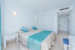 a white bedroom with a bed with blue pillows at Hostal Brisa Marina in Port d'Alcudia