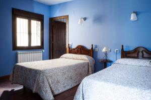 2 camas en una habitación con paredes azules y ventana en Ramajal Rural, en Horcajo