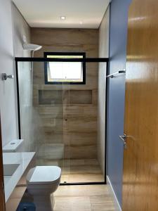a bathroom with a toilet and a glass shower door at Casa Pe na Agua Represa Igarata Piscina Climatizada in Igaratá