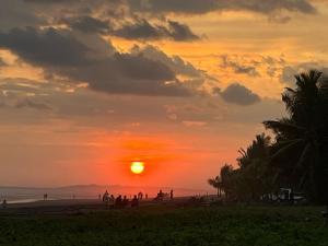 a sunset on a beach with a group of people at Bandera Beach Cabins in Parrita