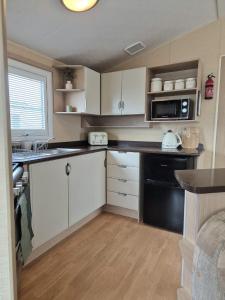 eine Küche mit weißen Schränken und einem schwarzen Gerät in der Unterkunft Meadow Lakes 64, pet friendly , WiFi & bed linen - Golden Palm Resort - Meadow Lakes Caravan & Lodge Hire in Chapel Saint Leonards