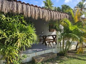 a patio with a table and a thatched roof at Suítes Milagres Bontempo in São Miguel dos Milagres