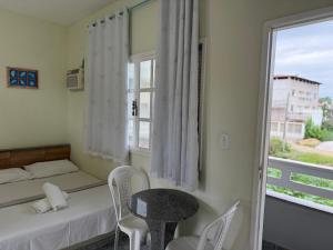 a bedroom with a bed and a table and a window at Pousada Tortuga in Anchieta