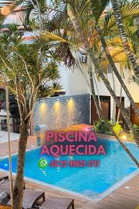 uma piscina com palmeiras em frente a um prédio em Pousada Estalagem dos Corais da Prainha em Arraial do Cabo