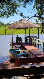 two people sitting at a dock with a hut on the water at Chalet del lago Don Asterio in Ciudad del Este