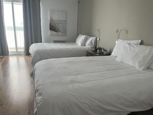 Dos camas en una habitación de hotel con sábanas blancas. en Hôtel Normandie, en Rimouski