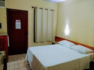 a bedroom with a white bed and a door at Patipe Praia Hotel in Canavieiras