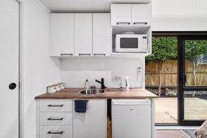 a white kitchen with a sink and a microwave at Cozy cabin near adventure spots! in Rotorua +1 photo