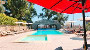 a pool with a red umbrella and chairs and a person sitting next to it at Hotel Bello by Ostello Bello in Finale Ligure