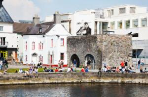 a group of people sitting on a wall near a body of water at 1 Minute to Everywhere! Galway City Centre in Galway