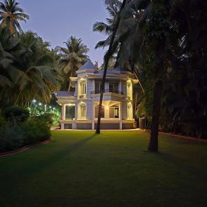 a large white house with palm trees on a lawn at Sea Breeze, Guhagar in Guhagar