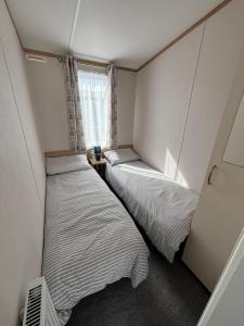 two beds in a small room with a window at Palm Grove 19 - Golden Palm - Central Heating, WiFi, pet friendly, bed linen - Meadow Lakes Caravan & Lodge Hire in Chapel Saint Leonards