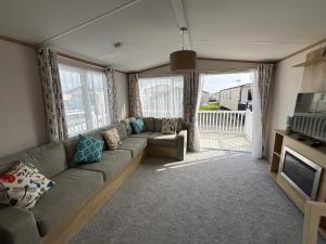 a living room with a couch and a television at Palm Grove 19 - Golden Palm - Central Heating, WiFi, pet friendly, bed linen - Meadow Lakes Caravan & Lodge Hire in Chapel Saint Leonards