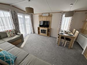 a living room with a couch and a table at Palm Grove 19 - Golden Palm - Central Heating, WiFi, pet friendly, bed linen - Meadow Lakes Caravan & Lodge Hire in Chapel Saint Leonards