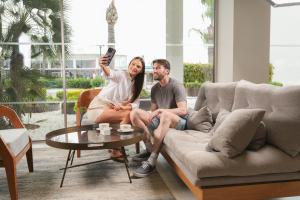 a man and woman sitting on a couch holding a cell phone at Faros Hotel Ayia Napa in Ayia Napa