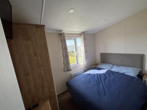 a bedroom with a blue bed and a window at Wildflower Meadows 5 - Golden Anchor - Central Heating, Wi-Fi, pet friendly, bed linen - Meadow Lakes Caravan & Lodge Hire in Chapel Saint Leonards