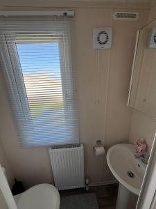 a bathroom with a toilet and a sink and a window at Wildflower Meadows 5 - Golden Anchor - Central Heating, Wi-Fi, pet friendly, bed linen - Meadow Lakes Caravan & Lodge Hire in Chapel Saint Leonards +3 photos