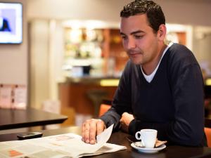 a man sitting at a table with a cup of coffee at Novotel Porto Gaia in Vila Nova de Gaia