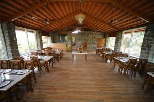 une salle à manger avec tables, chaises et fenêtres dans l'établissement Eshi Resorts and Restaurant - Bhimashankars Jungle Luxury Resort, à Taleghar