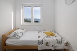 a white bedroom with a bed with a window at Apartman MORE Živogošće in Živogošće