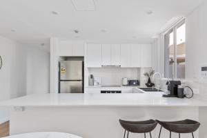 a white kitchen with white cabinets and two stools at Stylish 2-Bed Apartment with Pool in Camperdown in Sydney