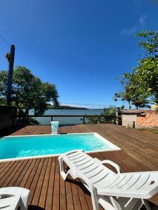 a deck with two white chairs and a swimming pool at Chalé com Hidromassagem, Lareira e Piscina na Beira da Lagoa in Imaruí