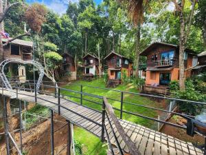 a bridge over a river in a forest with houses at บ้านต้นไม้แม่กำปอง Baan TONMAI MAEKAMPONG in Chiang Mai