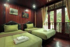two beds in a room with wooden walls and windows at Denchai City Resort เด่นชัยซิตี้ รีสอร์ท in Phrae