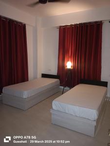 two beds in a room with red curtains at Rising Homestay in Guwahati