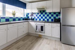 a kitchen with white cabinets and blue tiles at Stylish Home Near Addenbrookes Hospital by Traboule Properties Ltd in Shelford