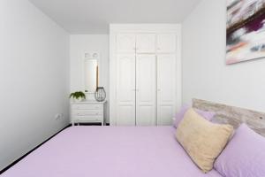 a white bedroom with a large bed with purple pillows at Ático San Juan Teide View in Playa de San Juan