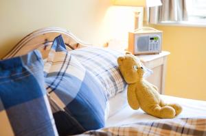 a teddy bear sitting on a bed with a pillow at The Dolphin Inn in Thorpeness