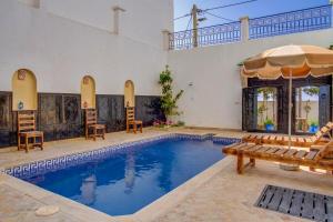 a swimming pool in a house with chairs and an umbrella at Berber riad with private pool in Aourir