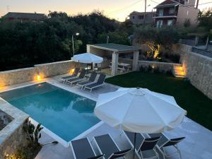 a pool with chairs and an umbrella and a table at Villa Eoli Corfu in Ágios Prokópios