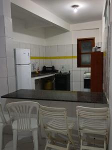 a kitchen with two white chairs and a counter with a refrigerator at Casas Cocos da Primeira Praia 2 in Cayru