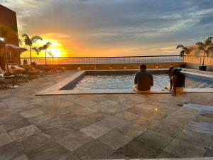 a group of people sitting around a swimming pool at sunset at Flat Privativo Sol Victoria Marina in Salvador