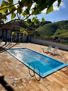 a swimming pool on a patio with two chairs at Pousada Doce Villa in Capitólio