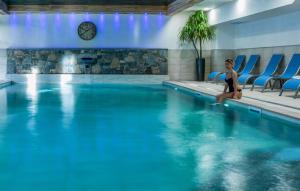 a woman sitting on the edge of a swimming pool at CGH Résidences & Spas Les Chalets De Laÿssia in Samoëns