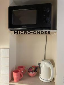 a microwave sitting on top of a shelf with cups at Prana Lodge Saint Gilles les Bains 800 m de la plage in Saint-Gilles-les-Bains