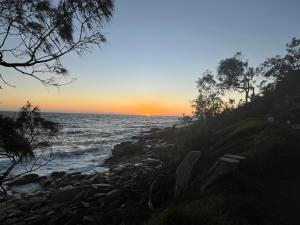 a sunset over the ocean with a rocky shore at South West Rocks Gap Beach Studio in Arakoon