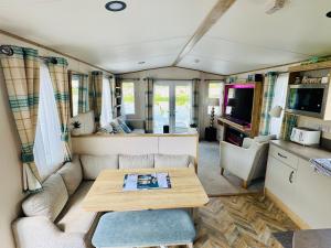 una sala de estar con sofá y mesa en una caravana en Exquisite Lake lodge in Hoburne Holiday Resort - Valentino Rose Lodge, en South Cerney