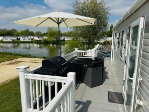un patio con sombrilla, mesa y parrilla en Exquisite Lake lodge in Hoburne Holiday Resort - Valentino Rose Lodge, en South Cerney