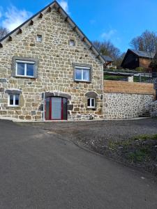 a stone house with a red door and a stone wall at Les Roses Des Bois in Murat-le-Quaire