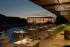 a restaurant with tables and chairs with a sunset in the background at Cala San Miguel Ibiza Resort, Adults only, Curio Collection by Hilton in Puerto de San Miguel