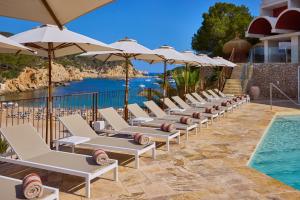 a row of lounge chairs with umbrellas next to a swimming pool at Cala San Miguel Ibiza Resort, Adults only, Curio Collection by Hilton in Puerto de San Miguel
