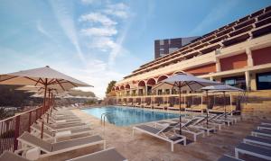 a pool with chairs and umbrellas next to a building at Cala San Miguel Ibiza Resort, Adults only, Curio Collection by Hilton in Puerto de San Miguel