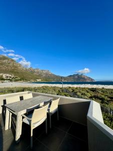 a wooden table and chairs on a balcony with the beach at Pingu Beachhouse with Jacuzzi Hout Bay Cape Town in Cape Town +64 photos