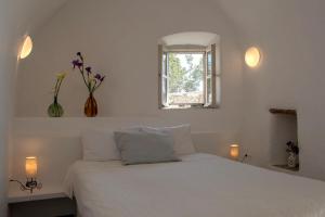 a white bedroom with a white bed with a window at Borantza stone house in Aroniadika